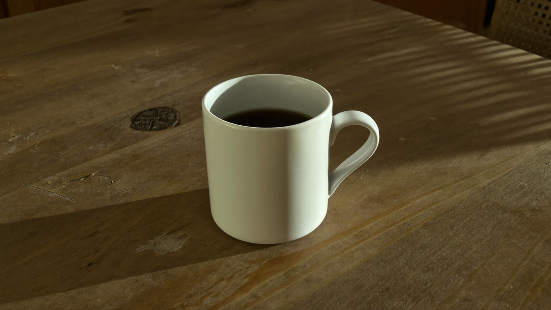 Wit kopje zwarte koffie op een houten tafel in het late middaglicht