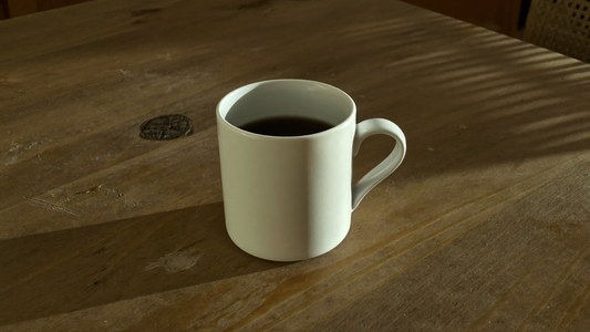 Wit kopje zwarte koffie op een houten tafel in het late middaglicht
